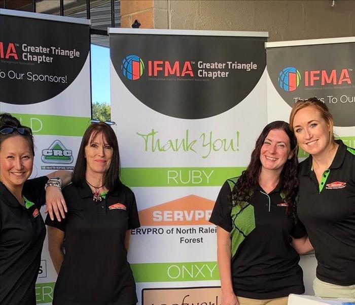 Four SERVPRO employees standing in front of a IFMA posters. 
