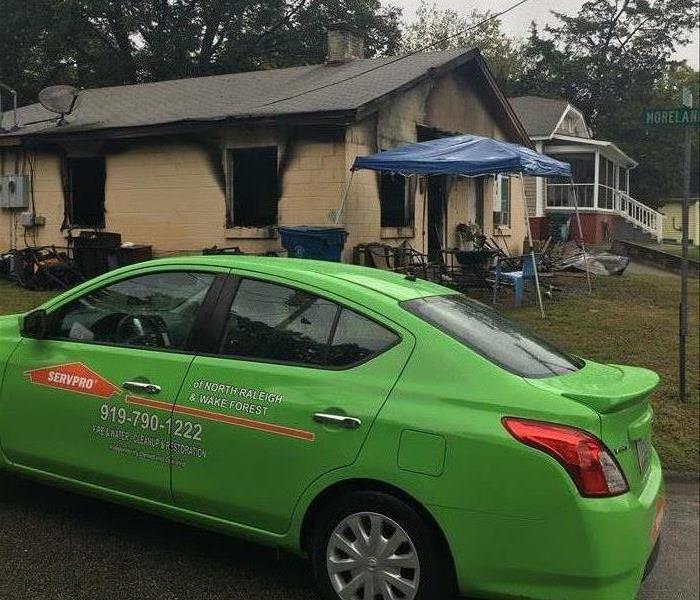 A SERVPRO vehicle parked in front of a house with fire damage.