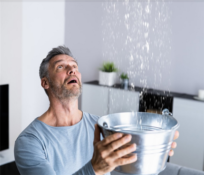 a man holding a bucket to catch water falling from the ceiling